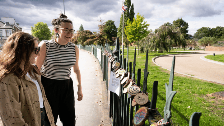 Two women looking at the crafts hung on the fence outside the William Morris gallery in Walthamstow