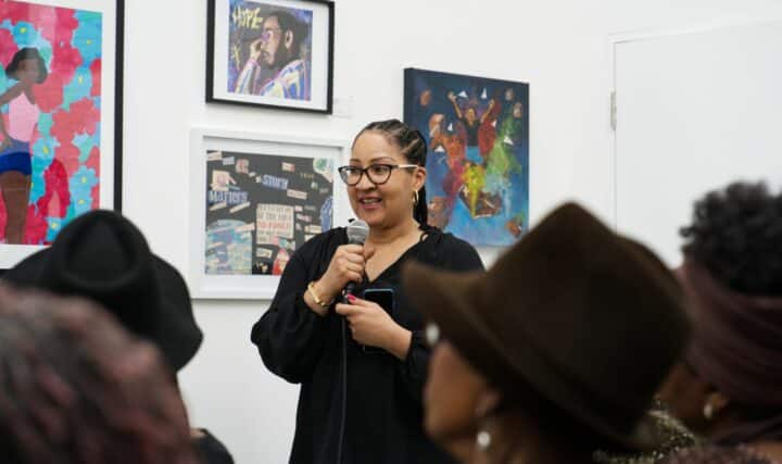 Vanessa speaks in front of a crowd with paintings behind her