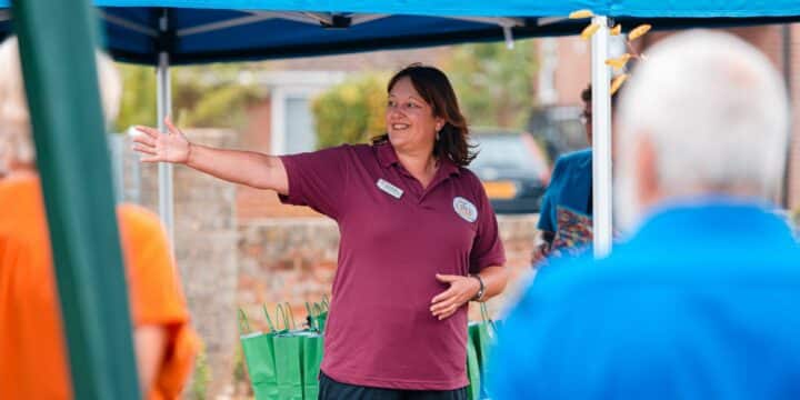 A woman stands talking in front of a crowd.