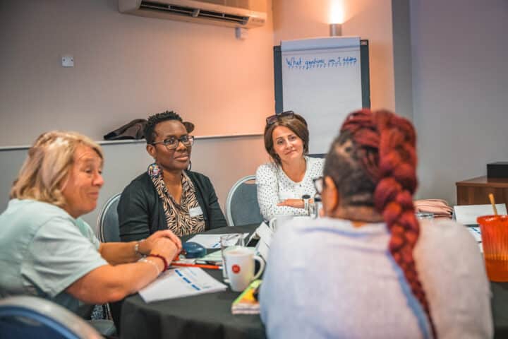 Four women sit round a table with a flip chart in the background