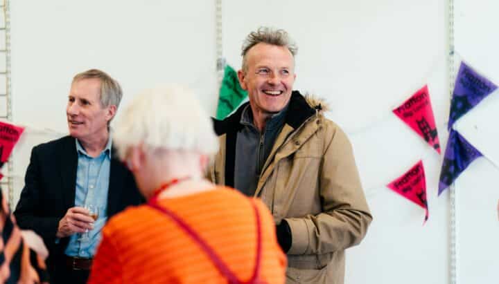 Man wearing brown jacket smiling with bunting hanging in the background
