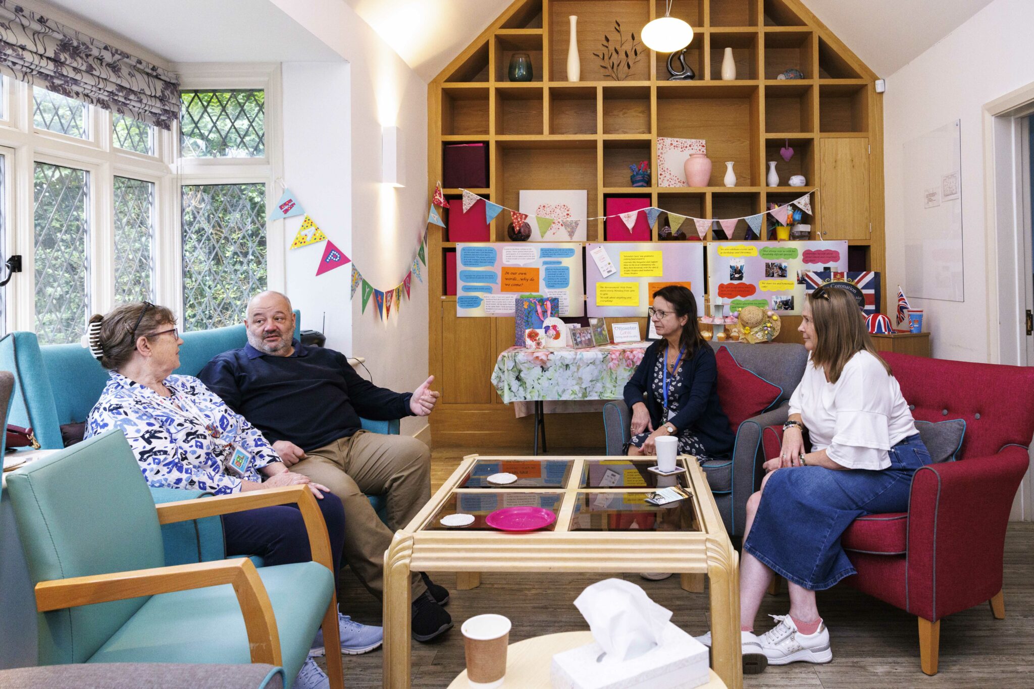 Four people sit together in armchairs in a community centre with bunting hung around the room