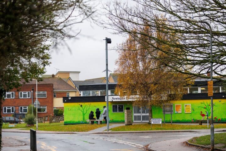 A bright green community centre with a sign half concealed by a large tree that reads 'Newington Community Centre'. It is a grey autumn day.